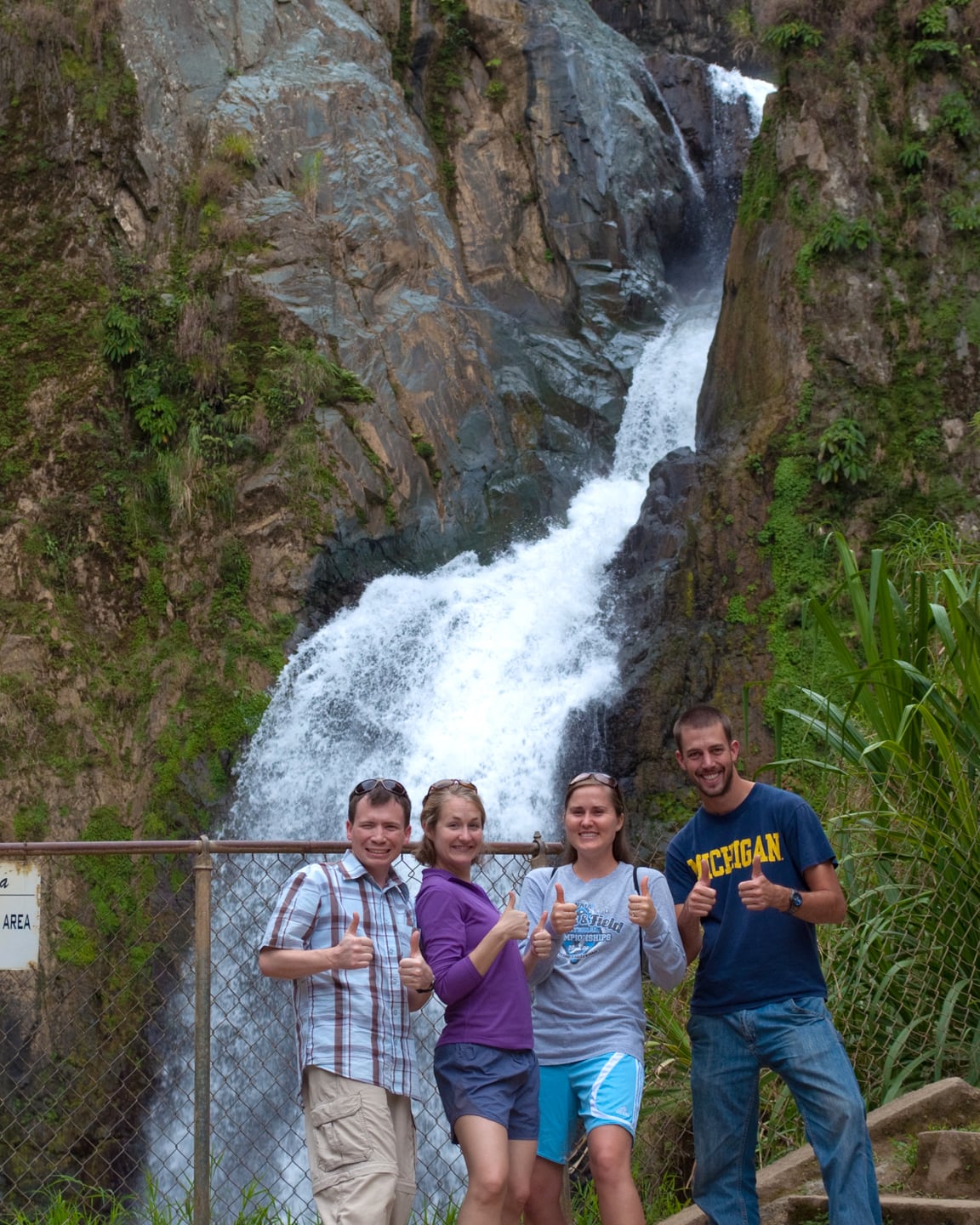 hikers standing in front of waterfall giving thumbs up