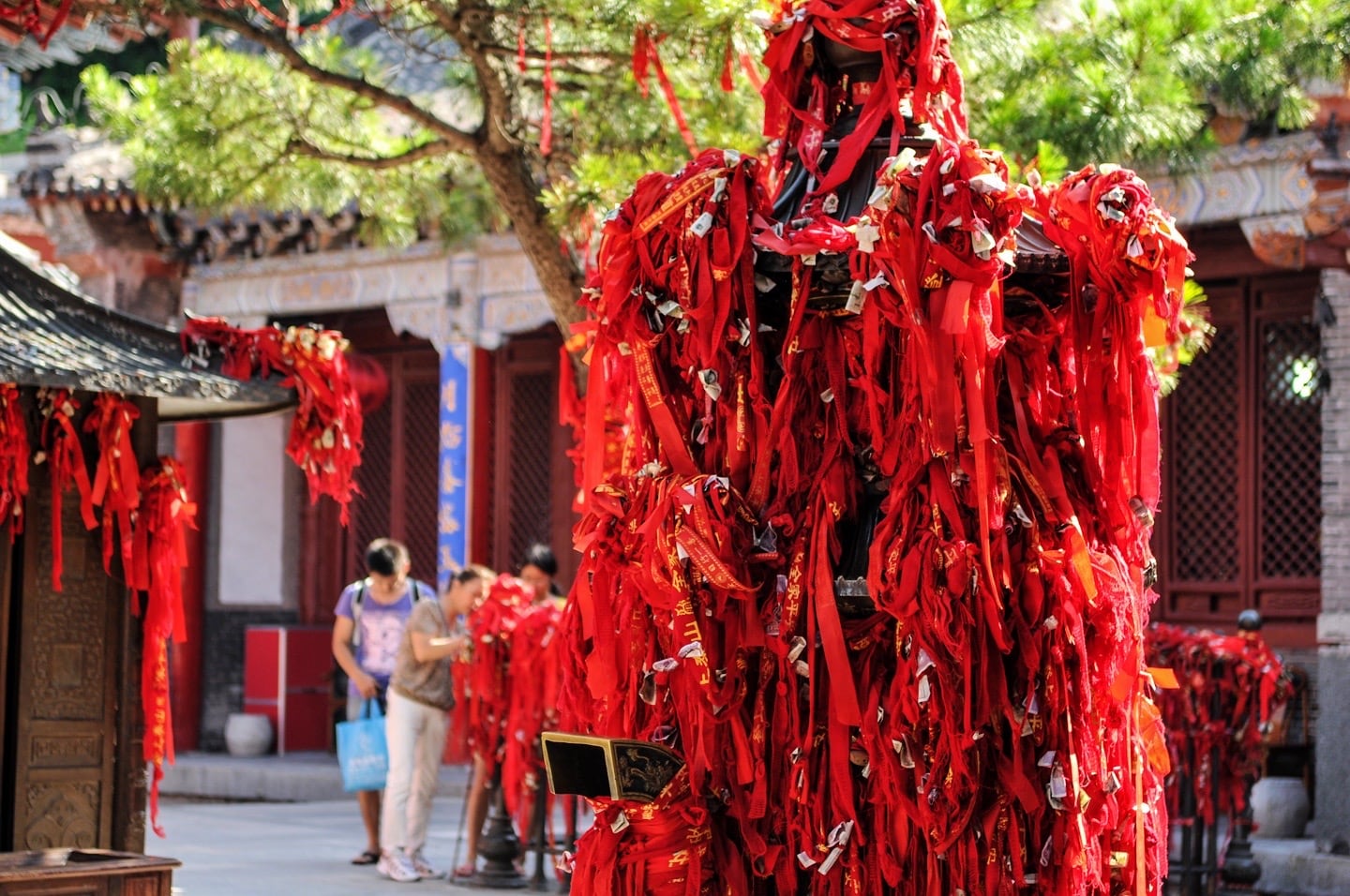 hundreds of red ribbons tied around a wooden pillar