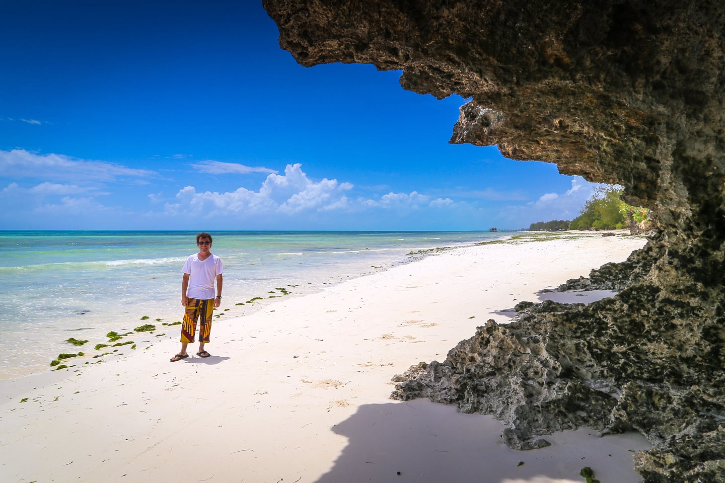 man standing on beach near coral rock formation