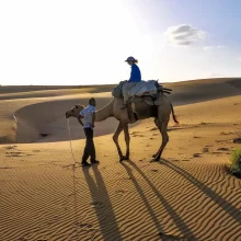 woman on camel with driver in Khuri Sand Dunes Jaisalmer Rajasthan India