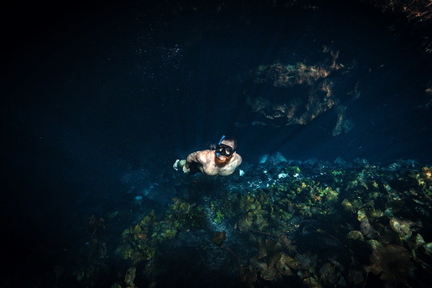 man snorkeling through underwater cave