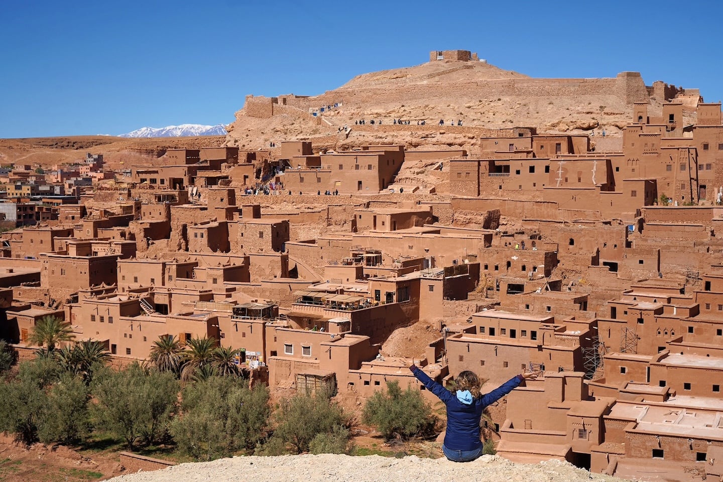 woman with hands up sitting on hill overlooking Ait Benhaddou ksar